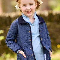 Little English traditional children's clothing. Long sleeve Hastings polo in light blue with ruffle collar and green floral detailing. Paired with green floral leggings for little girls with navy quilted jacket layered over