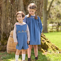 Little English traditional children's clothing. Khaki Gingham peter pan shirt for toddler boys paired with stormy blue corduroy shortall with flying mallard smocking across chest. Long sleeve stormy blue corduroy dress with flying mallard collar around the neckline for little girls.