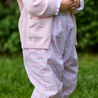 Little English traditional children's clothing. Light pink and green floral overall with ruffle detailing layered over white knit smocked Madeline Blouse in light pink. Light pink cotton bow pocket cardigan added on top.