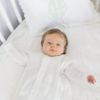 Little English traditional children's clothing. Unisex pleated ivory newborn gown with ruffles and embroidered detailing at the collar and sleeves. scallop pillow case and embroidered crib sheet in meadow green embroidery