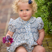 Little English classic children's clothing. Dressy peter pan bubble for baby girls in blue Wisteria Floral with puff sleeves, ruffle details, and smocking at chest.