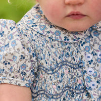 Little English classic children's clothing. Dressy peter pan bubble for baby girls in blue Wisteria Floral with puff sleeves, ruffle details, and smocking at chest.