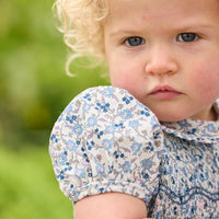 Little English classic children's clothing. Dressy peter pan bubble for baby girls in blue Wisteria Floral with puff sleeves, ruffle details, and smocking at chest.