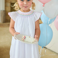 Little English traditional children's clothing. White flutter sleeve dress for toddler girls with rainbow smocking at the collar.  Birthday dress for little girls