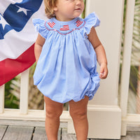 Little English traditional children's clothing.  Flutter sleeve bubble in royal blue mini check fabric and smocking with American flag bunting for baby girls