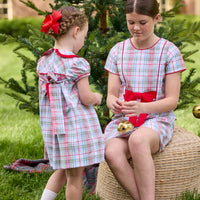 Little English classic children's clothing. Girls A-line dress in red and green plaid with red bow and red piping detail for the holidays.  Matching toddler girl dress with ruffled peter pan collar and bow tie sash in back.