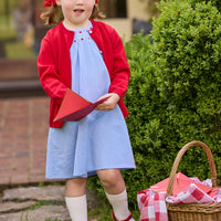 Little English traditional children's clothing. Soft blue chambray short sleeve dress for little girls with red and pink heart embroidery around the neckline. Red cotton cardigan layered on top.