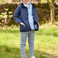 Little English traditional children's clothing.  Long sleeve Hastings polo in light blue with ruffle collar and green floral detailing. Paired with green floral leggings for little girls with navy quilted jacket layered over