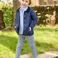 Little English traditional children's clothing.  Long sleeve Hastings polo in light blue with ruffle collar and green floral detailing. Paired with green floral leggings for little girls with navy quilted jacket layered over