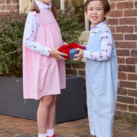 Little English classic children's clothing. White knit turtleneck with holiday train print layered under light blue corduroy Campbell Overall. White knit turtleneck with holiday present print layered under light pink corduroy Madison Jumper. Holiday outfit for little boys and girls.