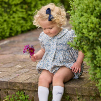 Little English classic children's clothing.  Dressy peter pan bubble for baby girls in blue Wisteria Floral with puff sleeves, ruffle details, and smocking at chest. Paired with white cotton knee high socks with navy bow embroidery