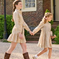 Little English traditional children's clothing. Long sleeve peter pan dress in tan Camden Floral with smocking across the chest for little girls. Older girls shirt dress in tan Camden Floral with long sleeves and tie sash at waist.