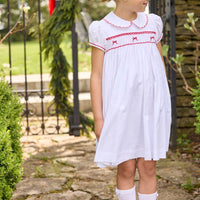 Little English traditional children's clothing.  Puff sleeve white peter pan dress with scalloped collar, red trim, and bow smocking across the chest.  Dressy outfit for little girls for the holiday