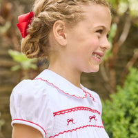 Little English traditional children's clothing.  Puff sleeve white peter pan dress with scalloped collar, red trim, and bow smocking across the chest.  Dressy outfit for little girls for the holiday