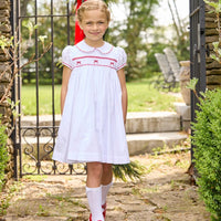 Little English traditional children's clothing.  Puff sleeve white peter pan dress with scalloped collar, red trim, and bow smocking across the chest.  Dressy outfit for little girls for the holiday
