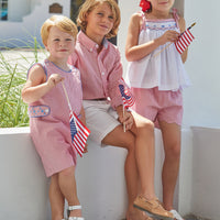 Little English girl's smocked top for Summer. Smocking with blue stars at center of chest and red seersucker gingham ties at shoulder for 4th of July.