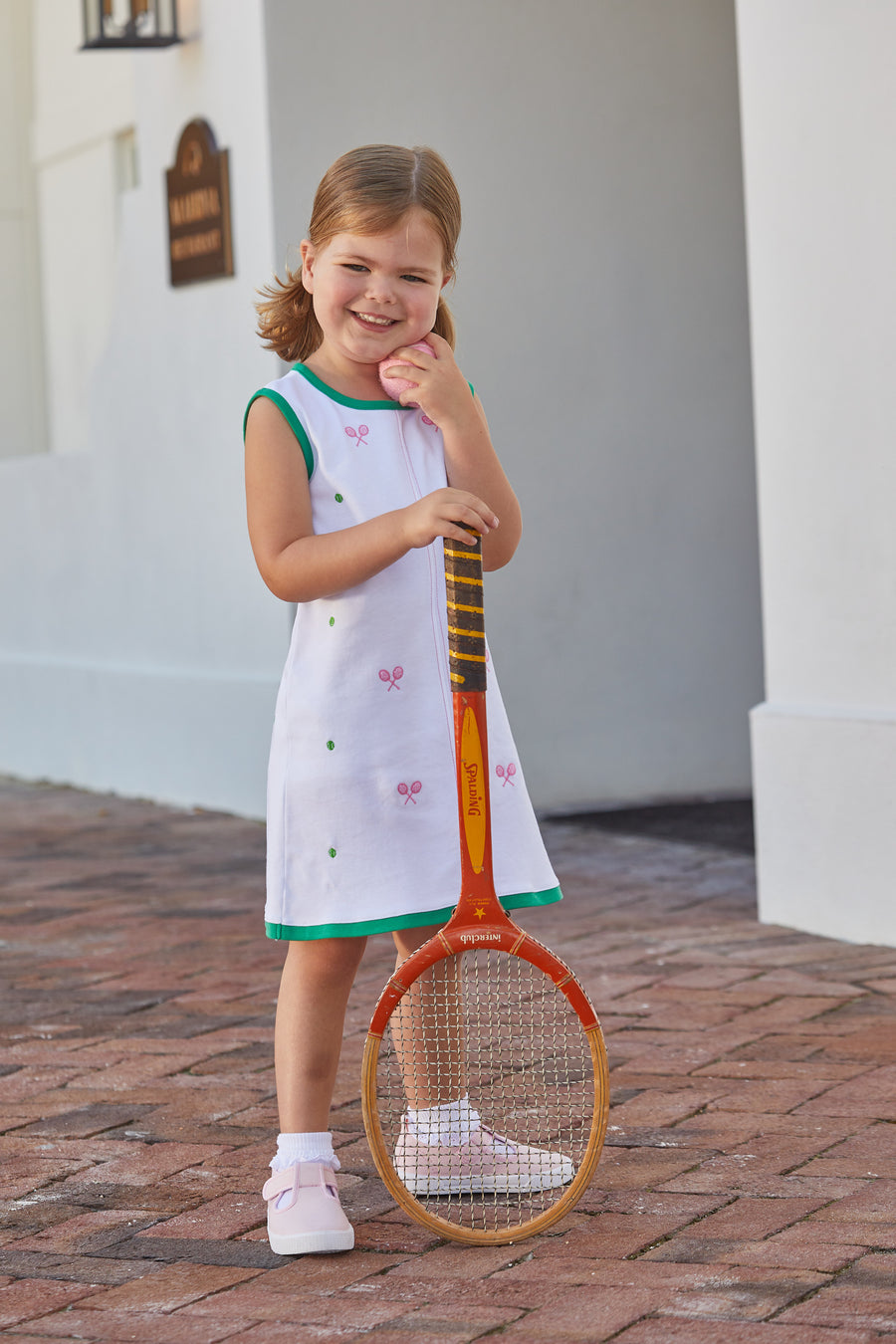 Little English traditional children's clothing, girl's casual white knit dress for Spring with green trim around the edges and pink and green tennis-themed embroidery